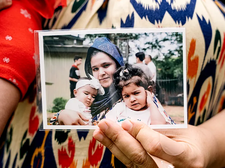 A refugee mother holds a photo of herself and her infant and toddler at an outdoor Friends of Refugees event.